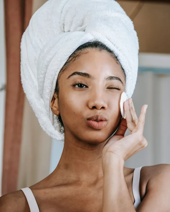 Une femme, une serviette sur les cheveux, applique un coton sur sa joue